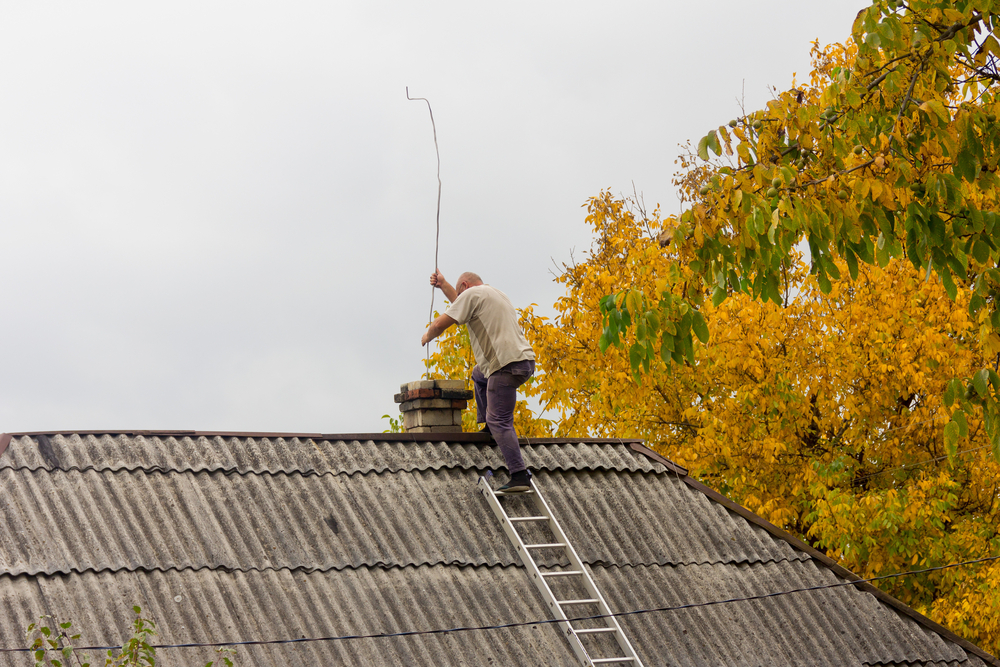 Male,Chimney,Sweep,Cleans,The,Chimney,On,The,Roof,Of