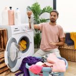 Handsome,Hispanic,Man,Doing,Laundry,Covering,Nose,For,Smelly,Sock