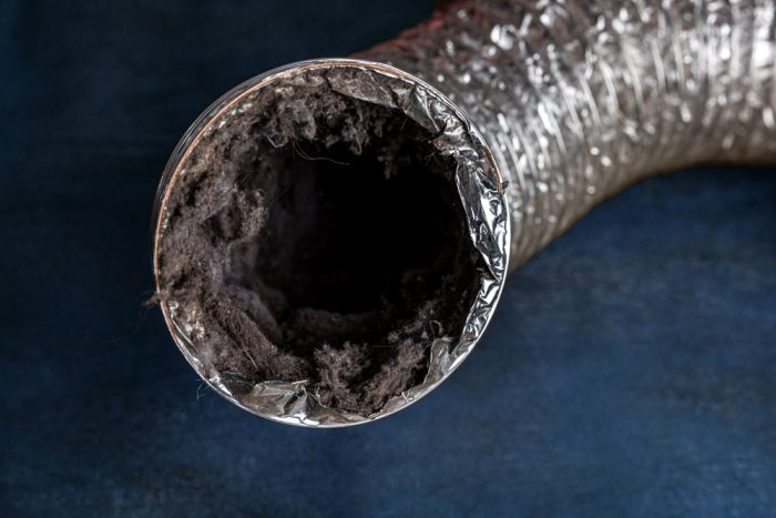 A dirty laundry flexible aluminum dryer vent duct ductwork filled with lint, dust and dirt against a blue background.